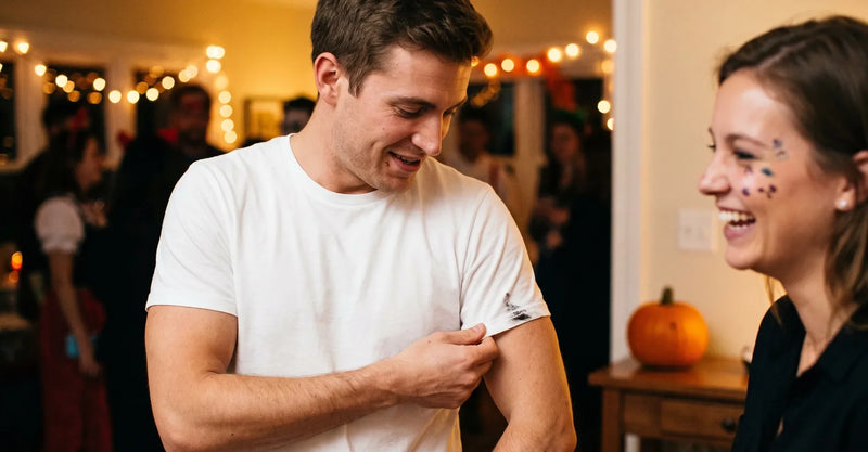 Man checking a mark on his white T-shirt sleeve at a Halloween party